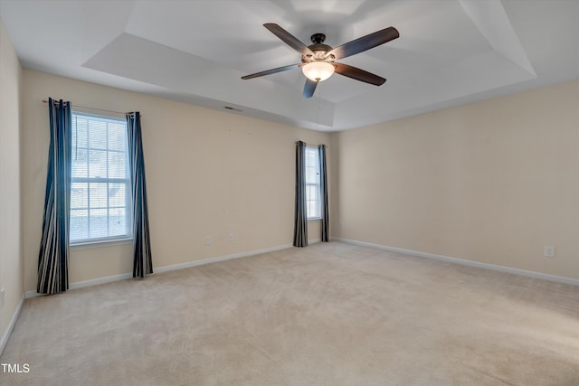 spare room with ceiling fan, a raised ceiling, and light carpet