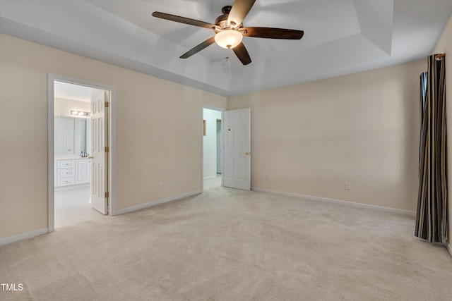 unfurnished bedroom featuring a tray ceiling, light colored carpet, ceiling fan, and ensuite bathroom