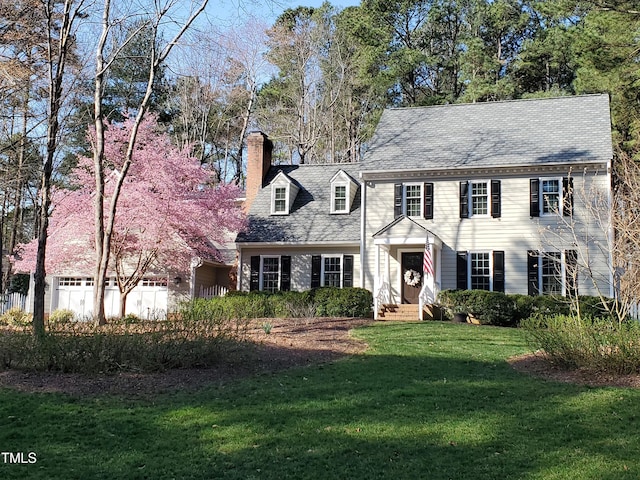 colonial house with a chimney, entry steps, a garage, and a front yard