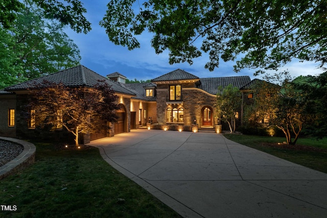 mediterranean / spanish-style home featuring a tile roof, concrete driveway, an attached garage, stone siding, and a front lawn