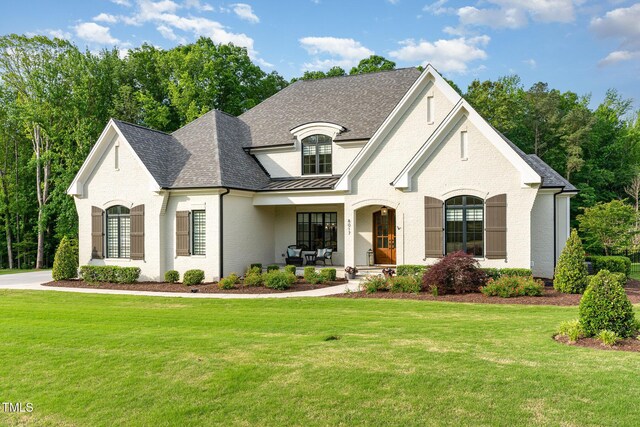french provincial home featuring a standing seam roof, a shingled roof, a porch, and a front yard