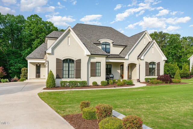 french provincial home with a shingled roof, concrete driveway, and a front lawn