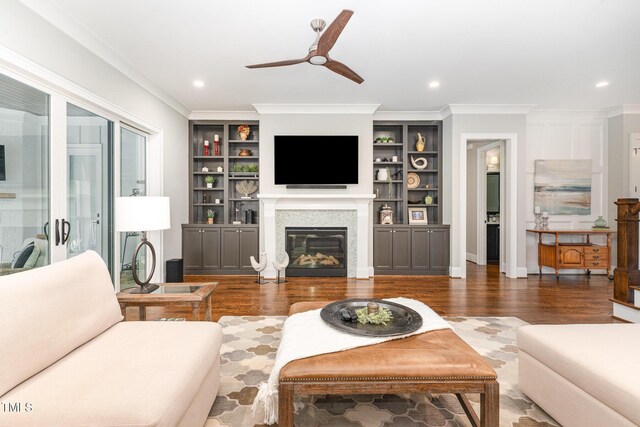 living area featuring a ceiling fan, crown molding, wood finished floors, baseboards, and a glass covered fireplace