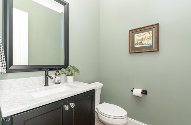 half bath featuring toilet, baseboards, and vanity