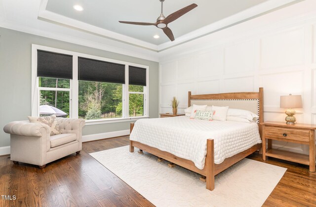 bedroom featuring a raised ceiling, a decorative wall, recessed lighting, and wood finished floors