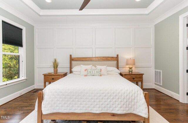bedroom with a tray ceiling, visible vents, dark wood-style floors, and a decorative wall