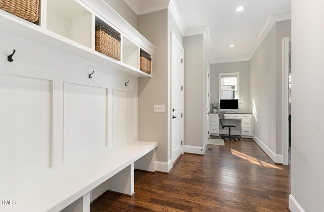 mudroom with crown molding, dark wood finished floors, built in desk, and baseboards