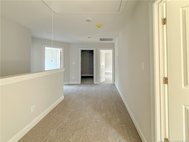 corridor featuring baseboards, visible vents, attic access, and light carpet