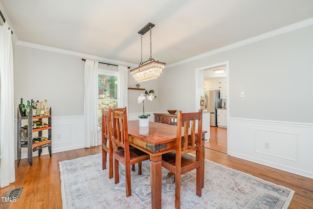 dining area with crown molding, visible vents, wainscoting, an inviting chandelier, and light wood-style flooring