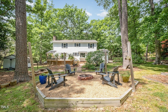 back of property with a fire pit, a deck, a chimney, an outbuilding, and a storage shed