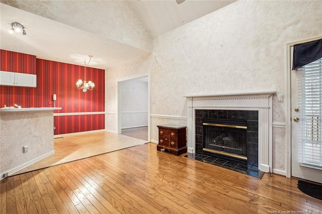 unfurnished living room with hardwood / wood-style flooring, lofted ceiling, a tiled fireplace, and an inviting chandelier