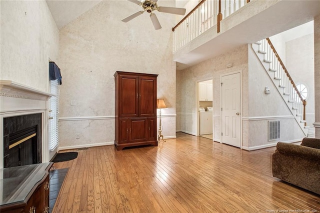 living room featuring a high ceiling, ceiling fan, washer and dryer, and light wood-type flooring