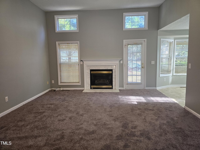 unfurnished living room with carpet floors, a high end fireplace, a wealth of natural light, and baseboards