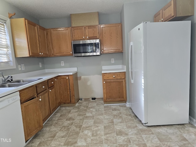 kitchen with brown cabinets, white appliances, light countertops, and a sink