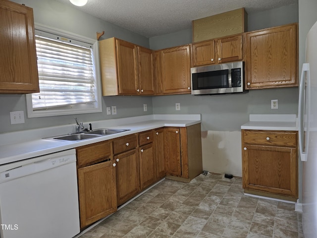 kitchen with light countertops, white appliances, brown cabinetry, and a sink