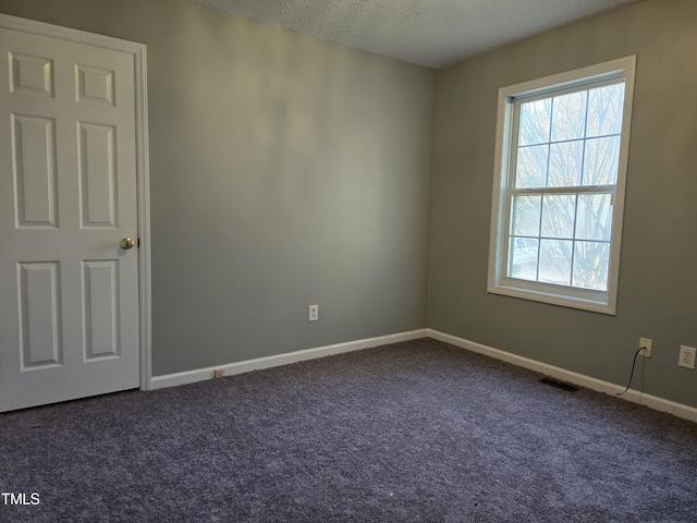 empty room with baseboards, visible vents, dark carpet, and a textured ceiling