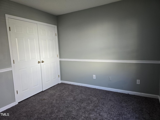 unfurnished bedroom with baseboards, dark colored carpet, and a closet