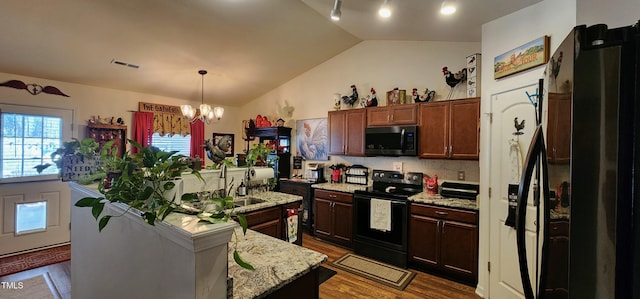 kitchen featuring pendant lighting, light stone counters, black appliances, an island with sink, and vaulted ceiling