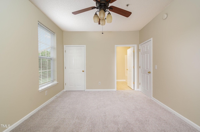 unfurnished bedroom with light carpet, ceiling fan, ensuite bath, and a textured ceiling