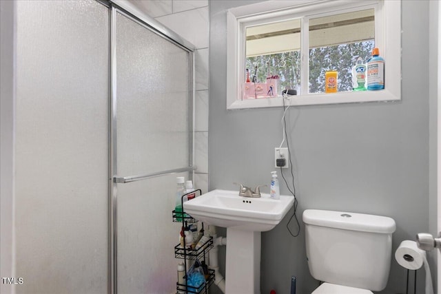 bathroom featuring a shower with shower door, sink, and toilet