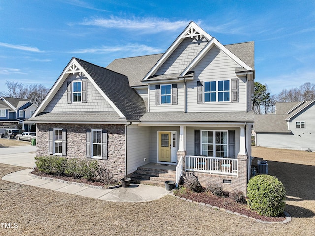 craftsman-style home with stone siding, a porch, roof with shingles, and central air condition unit