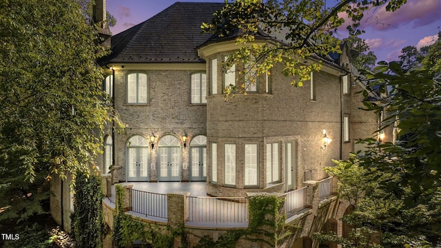 back house at dusk with french doors and a balcony