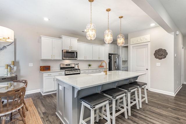 kitchen with an island with sink, appliances with stainless steel finishes, decorative light fixtures, white cabinetry, and a sink