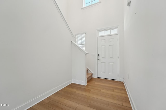 foyer entrance featuring a high ceiling, light wood finished floors, stairs, and baseboards