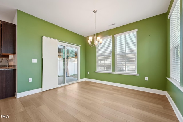 unfurnished dining area with visible vents, light wood-style flooring, an inviting chandelier, a sink, and baseboards