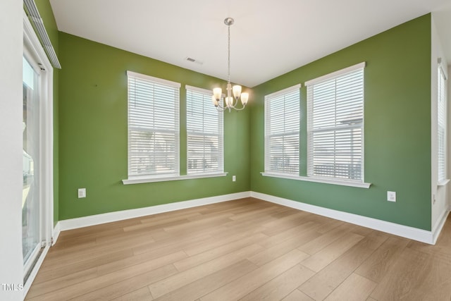 empty room featuring baseboards, light wood-style flooring, visible vents, and a notable chandelier