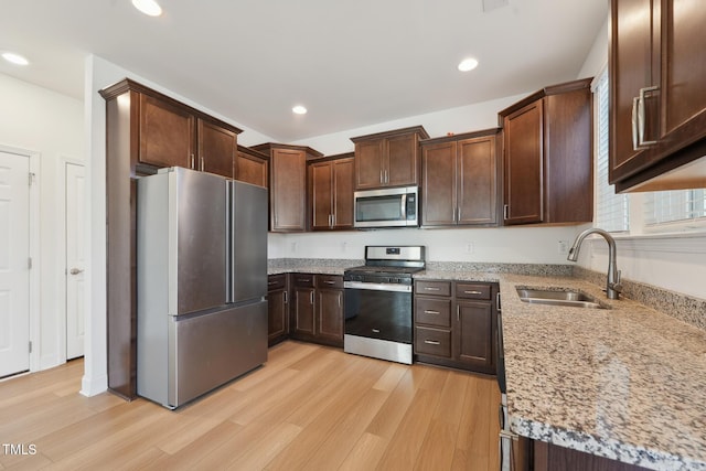 kitchen featuring appliances with stainless steel finishes, light stone counters, light wood-style floors, a sink, and recessed lighting