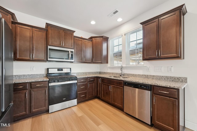 kitchen featuring light stone counters, recessed lighting, a sink, appliances with stainless steel finishes, and light wood finished floors