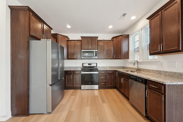 kitchen with light wood-style flooring, light stone countertops, stainless steel appliances, a sink, and recessed lighting