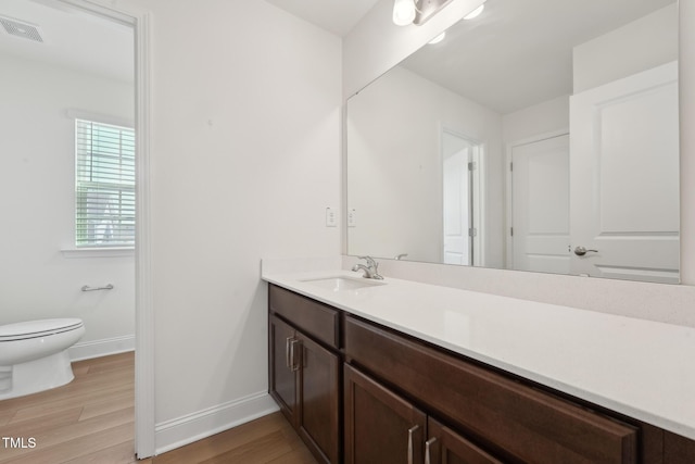 bathroom featuring toilet, wood finished floors, vanity, visible vents, and baseboards