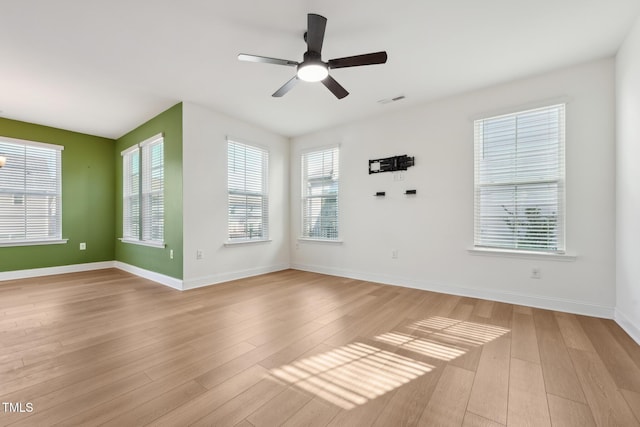 empty room with ceiling fan, light wood finished floors, visible vents, and baseboards