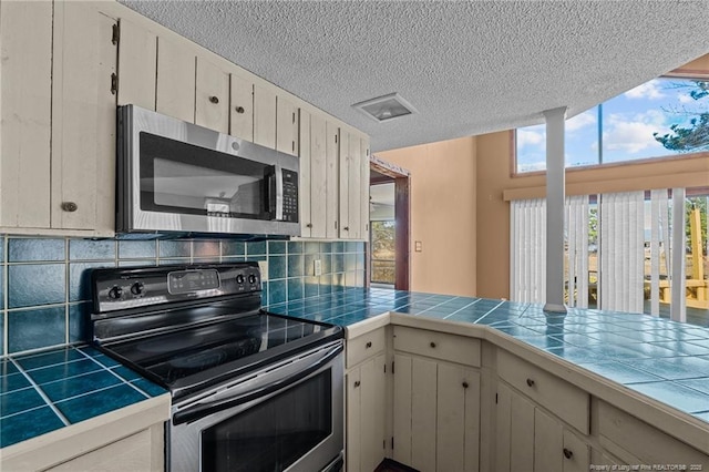 kitchen with appliances with stainless steel finishes, tile counters, a textured ceiling, and backsplash