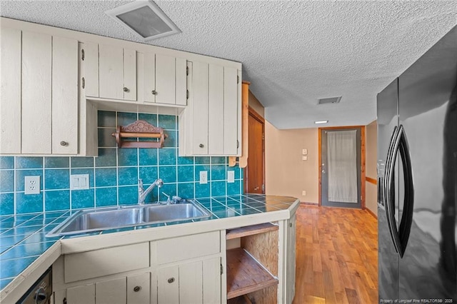 kitchen featuring sink, tile countertops, white cabinets, and black fridge