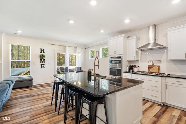 220 Green Haven Blvd, Youngsville, NC 27596 - kitchen featuring decorative backsplash, appliances with stainless steel finishes, light wood-style floors, and wall chimney exhaust hood