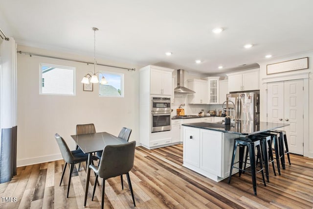 220 Green Haven Blvd, Youngsville, NC 27596 - kitchen with stainless steel appliances, dark countertops, light wood-style floors, a breakfast bar area, and wall chimney range hood