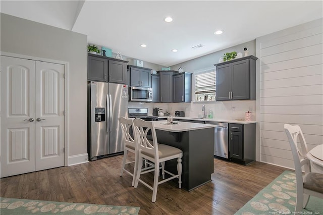 kitchen with a kitchen bar, dark hardwood / wood-style floors, gray cabinets, a kitchen island, and stainless steel appliances