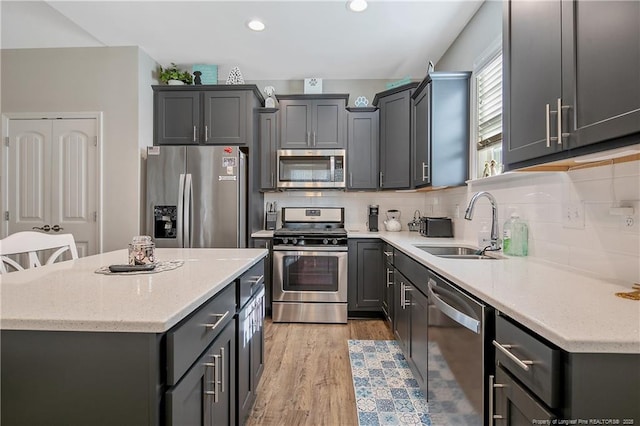 kitchen with sink, appliances with stainless steel finishes, a kitchen breakfast bar, tasteful backsplash, and light hardwood / wood-style floors