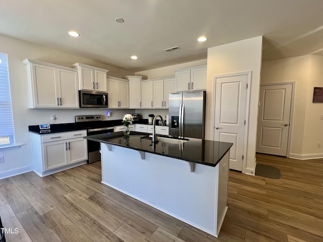 kitchen featuring a kitchen bar, sink, white cabinetry, stainless steel appliances, and a kitchen island with sink