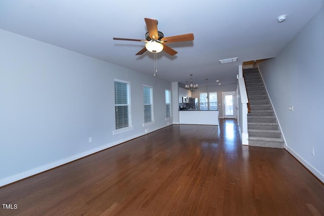 unfurnished living room with baseboards, visible vents, dark wood-style flooring, stairs, and ceiling fan with notable chandelier