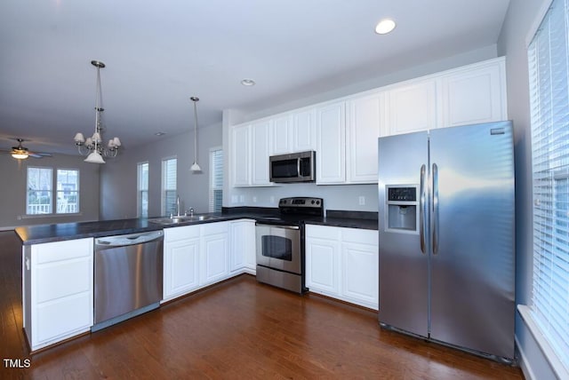 kitchen with dark countertops, stainless steel appliances, a peninsula, and a sink