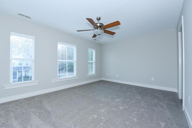 spare room featuring plenty of natural light, visible vents, dark colored carpet, and baseboards