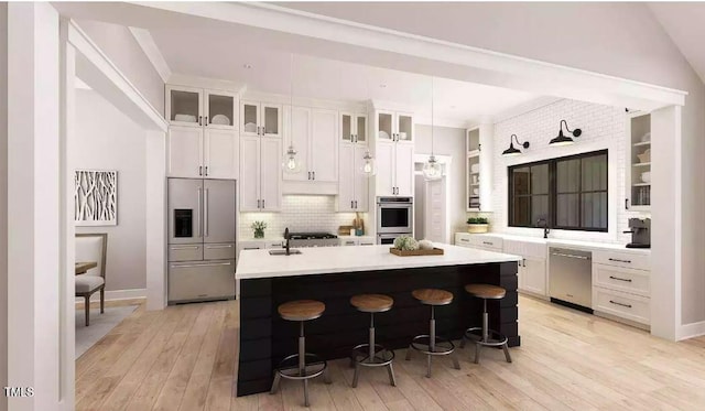 kitchen with a breakfast bar area, hanging light fixtures, an island with sink, stainless steel appliances, and white cabinets