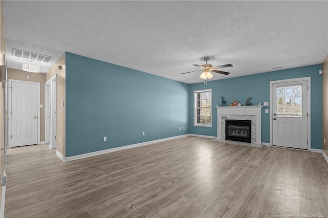 unfurnished living room featuring ceiling fan, a fireplace, light hardwood / wood-style floors, and a wealth of natural light