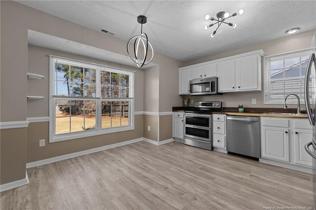 kitchen with stainless steel appliances, white cabinetry, sink, and butcher block countertops