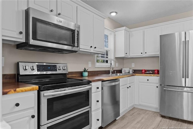 kitchen featuring sink, wooden counters, white cabinetry, stainless steel appliances, and light hardwood / wood-style floors