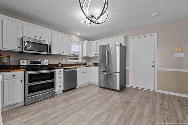 kitchen with appliances with stainless steel finishes, white cabinetry, light hardwood / wood-style floors, a textured ceiling, and wood counters